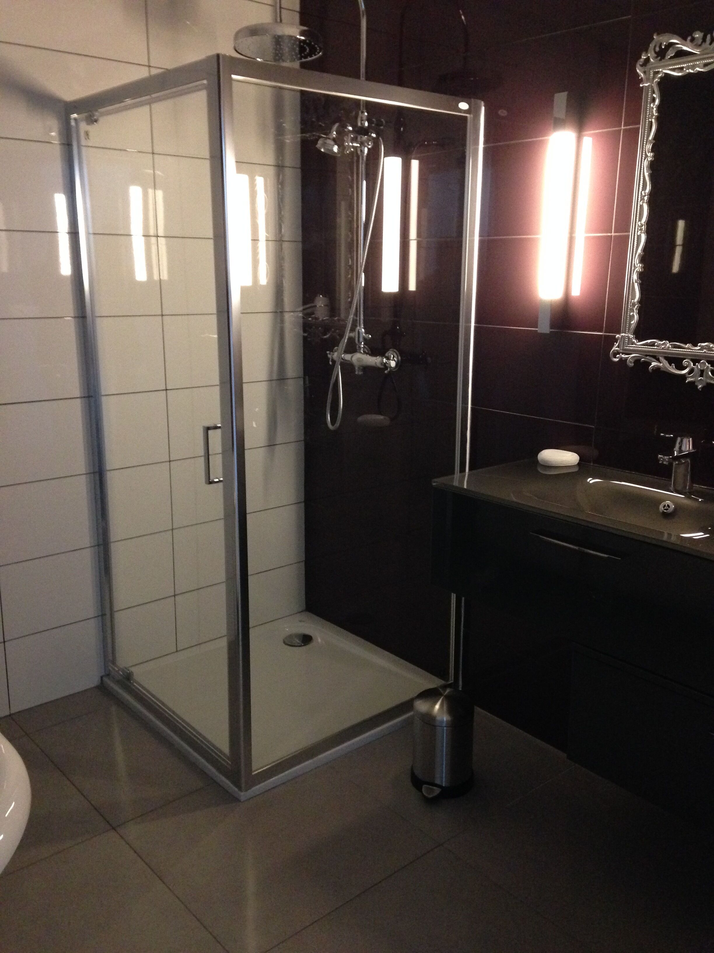 Une salle de bain moderne avec une douche à parois de verre, un meuble-lavabo foncé et un miroir doté d’un cadre orné.