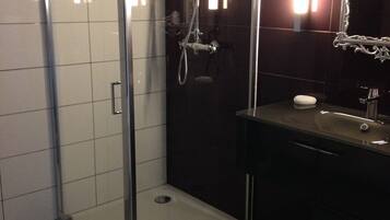 Une salle de bain moderne avec une douche à parois de verre, un meuble-lavabo foncé et un miroir doté d’un cadre orné.