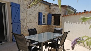 An outdoor patio with a glass table and four chairs, a stone wall, and blue shutters. - Family 2-bedroom gîte - Cognac countryside, pool, games room, pet friendly (Segonzac)