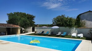 A swimming pool with lounge chairs and umbrellas, surrounded by a garden and a building. - Family 2-bedroom gîte - Cognac countryside, pool, games room, pet friendly (Segonzac)