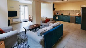 A living room with a sofa, a coffee table, and a TV. There is a kitchen with a microwave, stove, and cabinets. - Family 2-bedroom gîte - Cognac countryside, pool, games room, pet friendly (Segonzac)