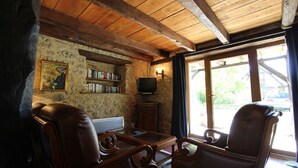 Une pièce rustique avec des poutres en bois, des fauteuils en cuir, une bibliothèque et un téléviseur.