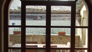 Une vue à travers une grande fenêtre en arc sur un espace de restauration comprenant plusieurs tables et chaises, un banc et des plantes en pot.