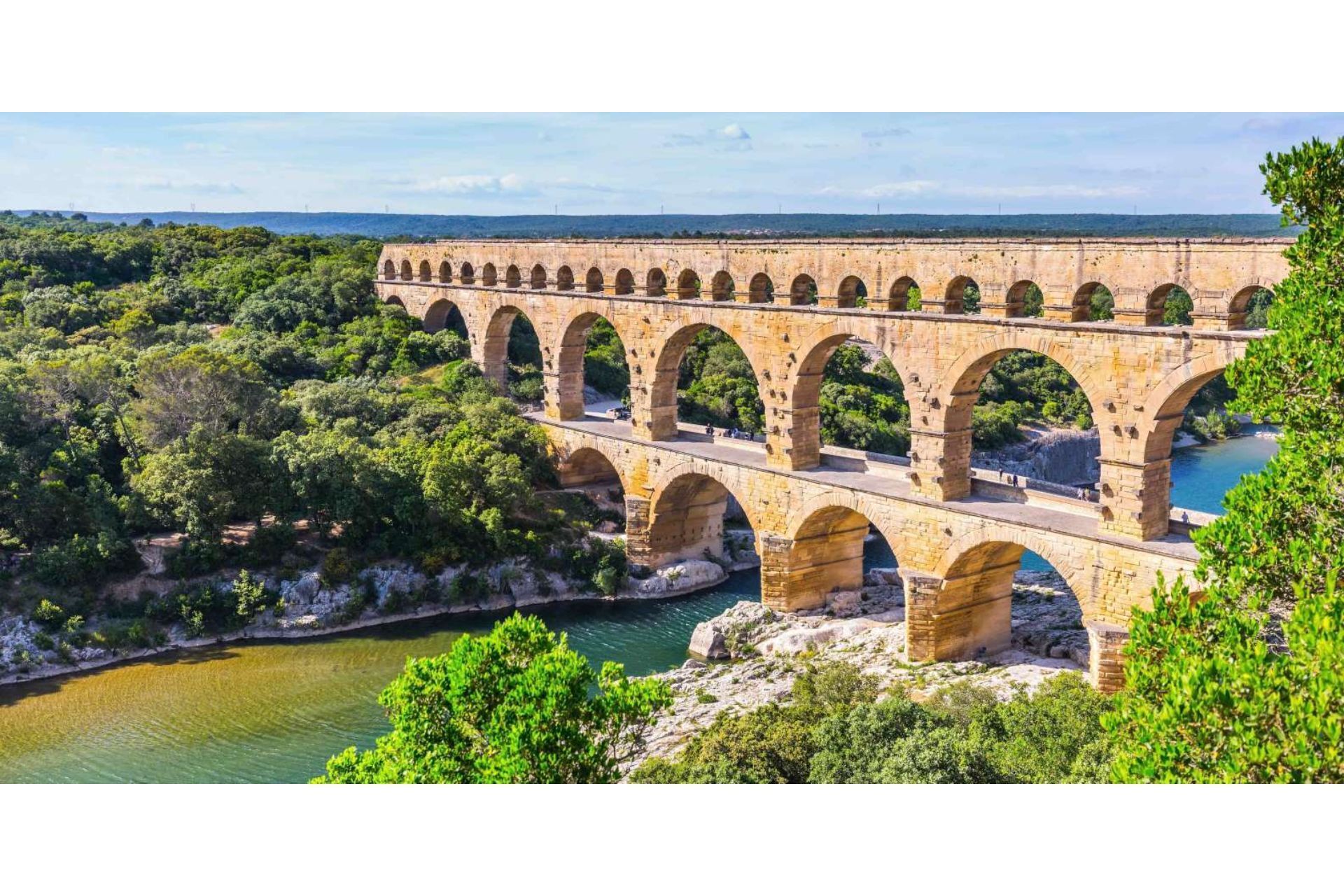 Un puente de acueducto de piedra sobre un río, rodeado de abundante vegetación.
