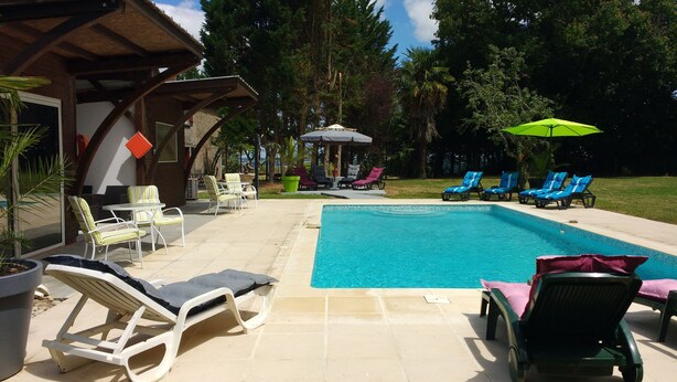Une piscine entourée d’arbres et agrémentée de transats, de parasols et d’un belvédère.