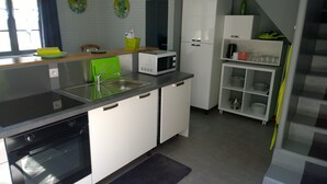 Une cuisine moderne équipée d’un lave-vaisselle, d’un four, d’un four à micro-ondes et d’un évier avec un robinet vert. On y trouve également un petit réfrigérateur et une étagère avec de la vaisselle.