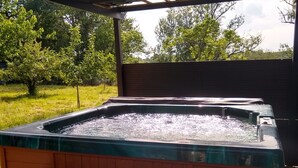 Un bain à remous avec des marches menant à celui-ci, entouré d’une terrasse en bois et d’un espace abrité.