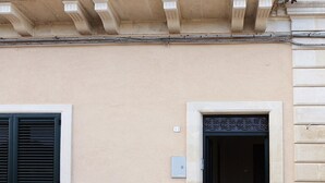 Eine auffällige Fassade mit einer beigefarbenen Wand, einem Fenster mit schwarzen Rollläden und einer Tür mit dekorativem Metallrahmen.