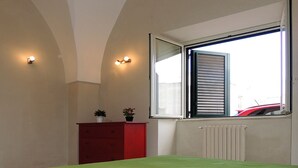 Ein Schlafzimmer mit Bett, Schminktisch, Fenster mit Jalousien und Heizkörper.