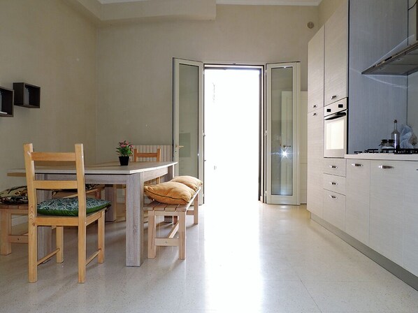 A modern kitchen with white cabinets, a dining table with chairs, and a view to the outside.
