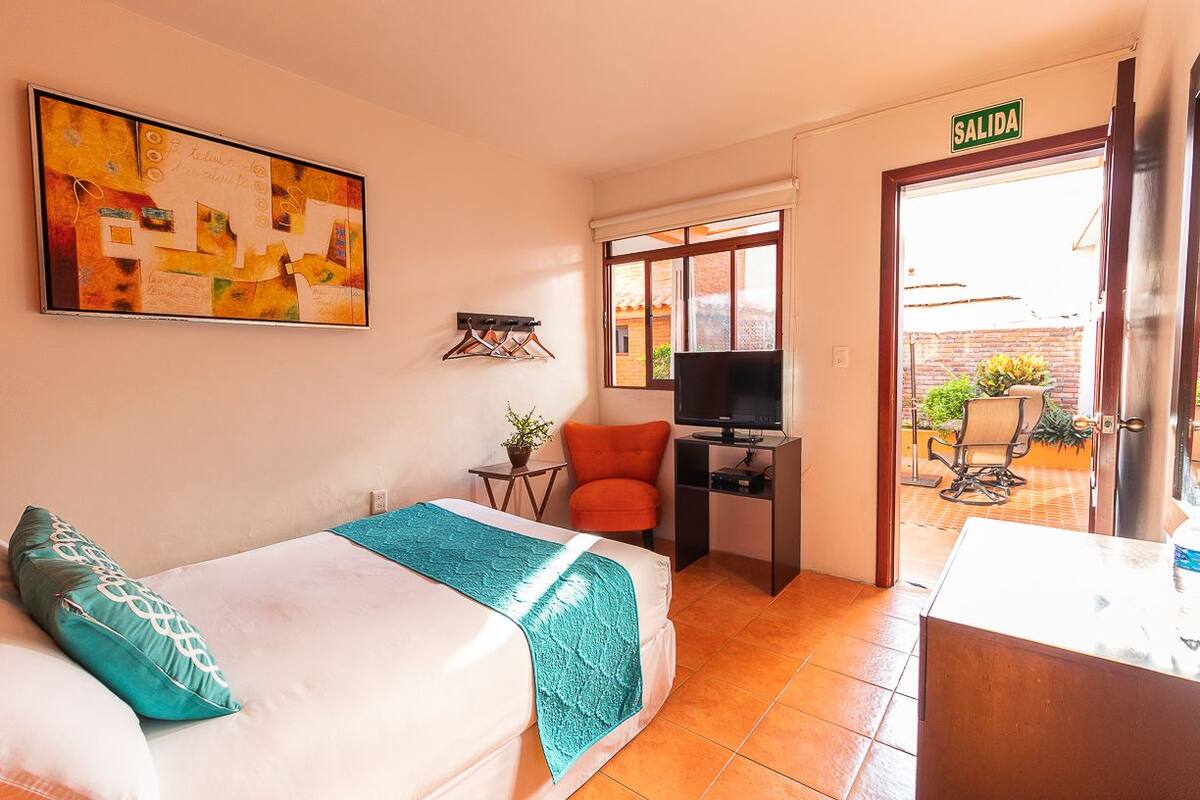 A hotel room with a bed, a desk, a TV, and a view of the outside.