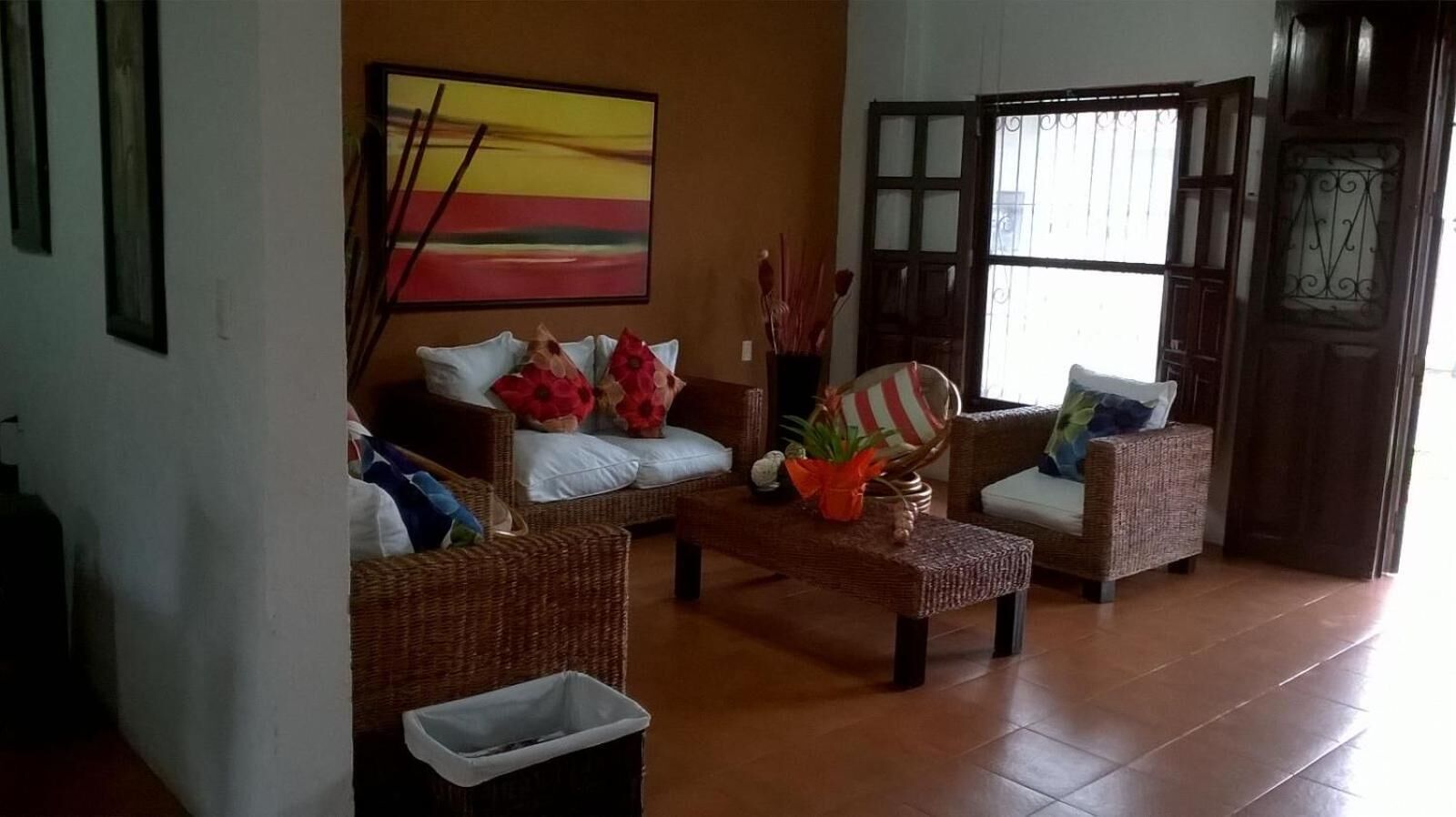 A living room with wicker furniture, a painting on the wall, and a window with bars.