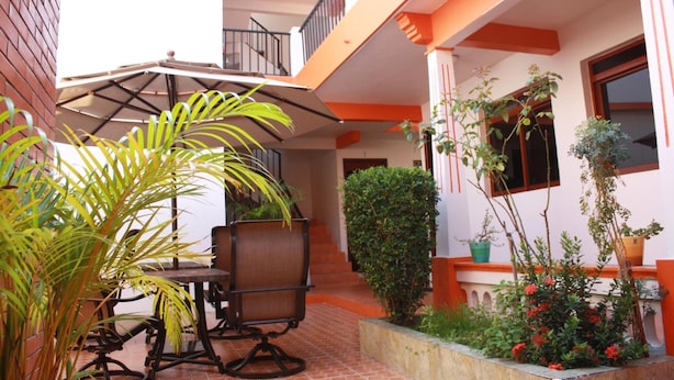 Un patio con una mesa y sillas para comer, rodeado de plantas en macetas y una escalera que sube a un nivel superior.