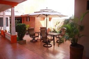An outdoor patio with a table and chairs, a large umbrella, and potted plants.