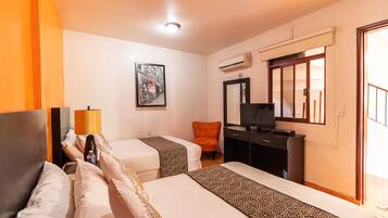 Habitación de hotel con dos camas, un escritorio con televisor, aire acondicionado y ventana con vista.