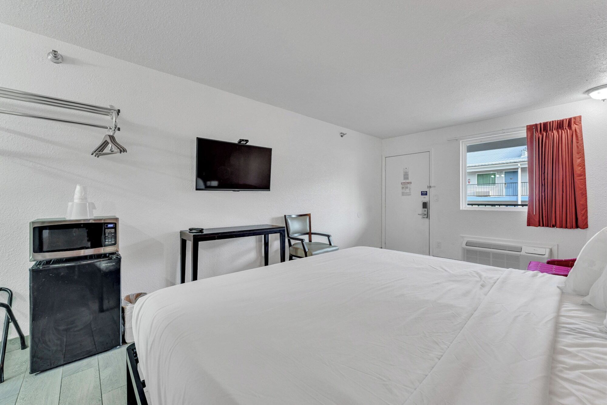 Une chambre d’hôtel équipée d’un lit, d’un téléviseur fixé au mur, d’un four à micro-ondes, d’une chaise et d’une fenêtre avec des rideaux.