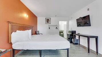 Habitación de hotel con una cama grande, un escritorio, una silla y un televisor montado en la pared.