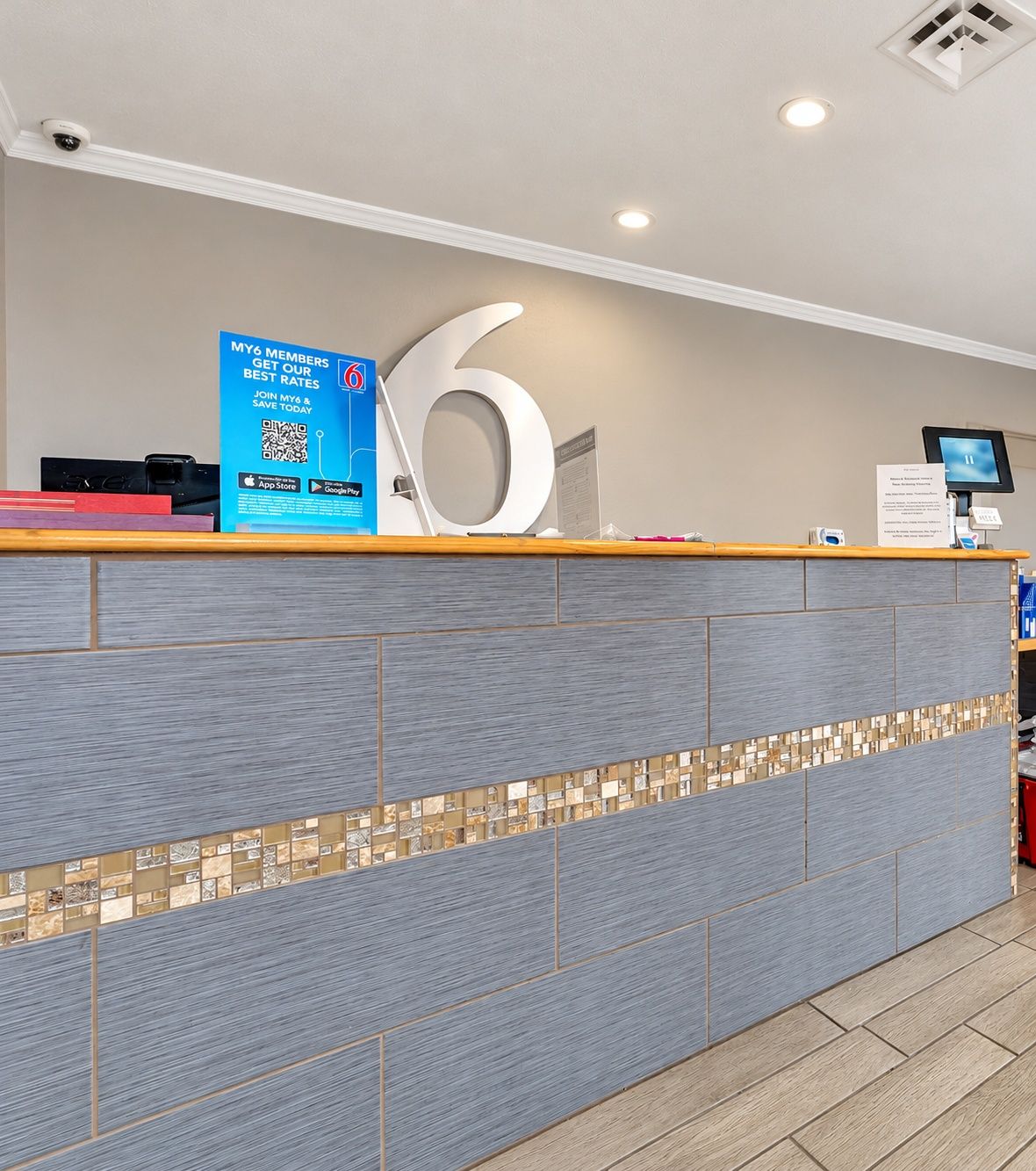 Un comptoir d’accueil avec un grand panneau indiquant le chiffre « 6 », un panneau publicitaire bleu et un écran d’ordinateur.