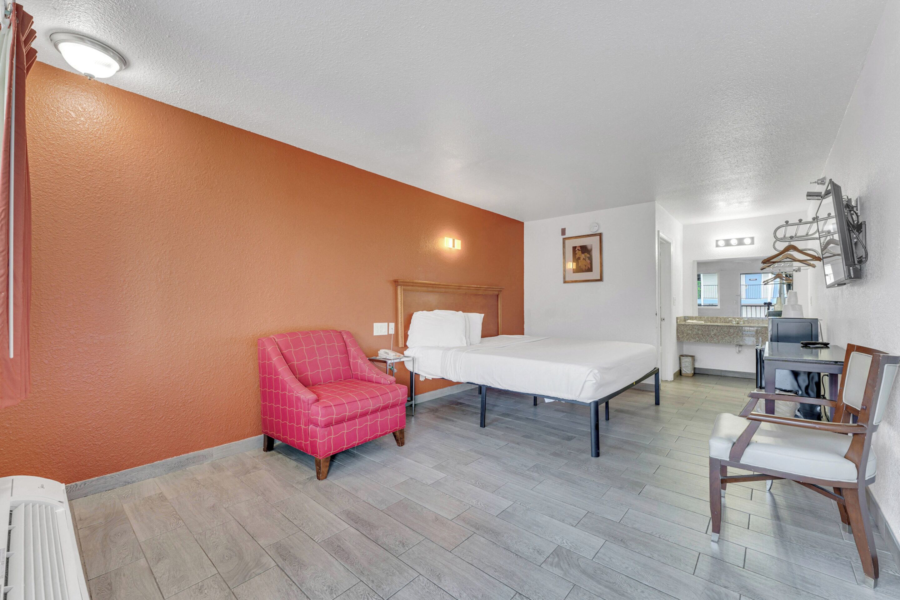 Habitación de hotel con cama, una silla, un escritorio y kitchenette.