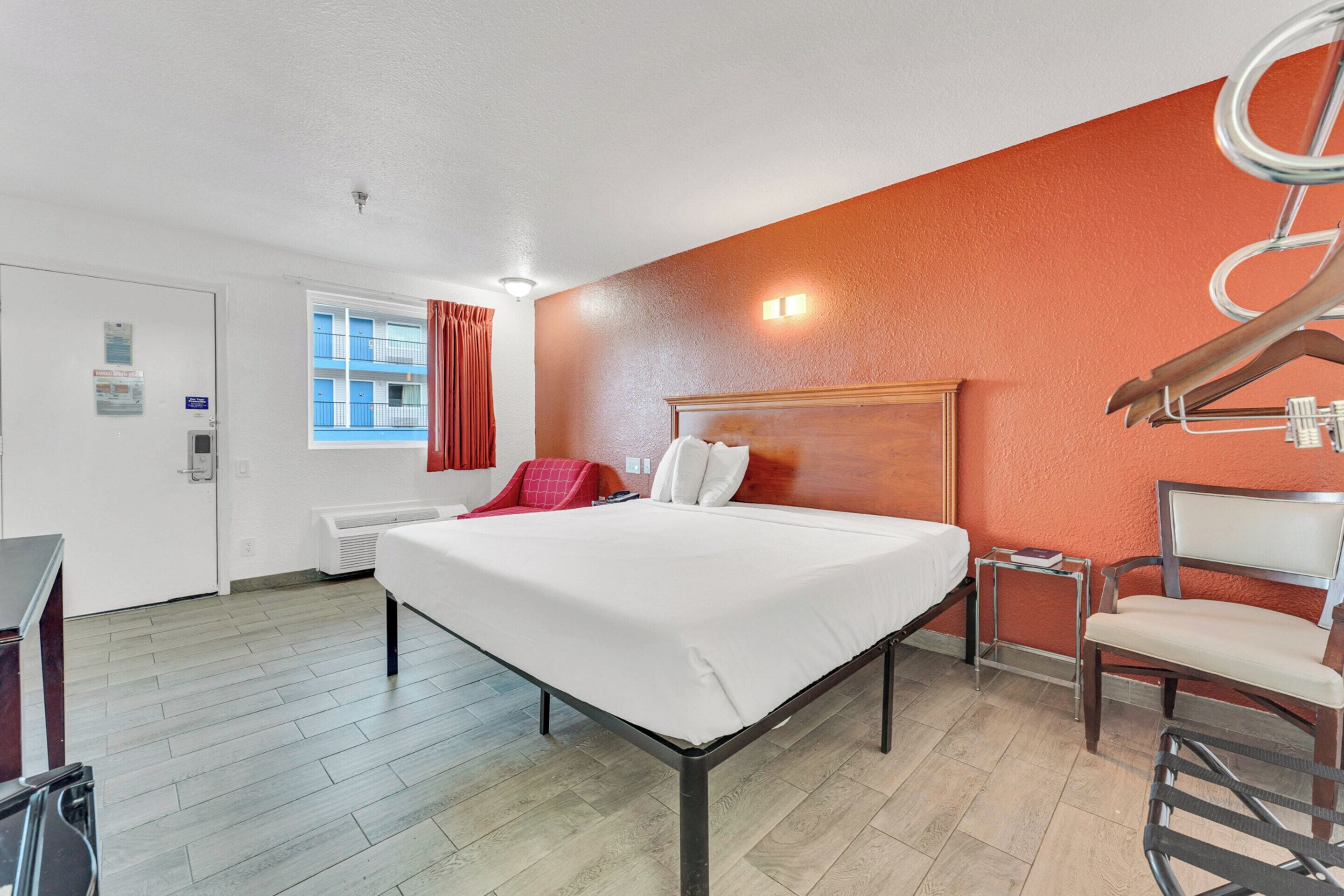 A hotel room with a bed, a chair, a desk, and a window with curtains.