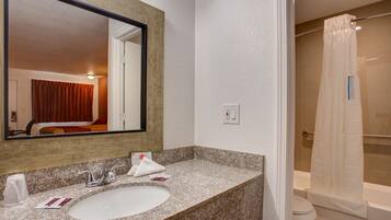 Une salle de bain d’hôtel avec un lavabo doté d’un plan de travail en granit, un grand miroir, un rideau de douche et des toilettes bien visibles.