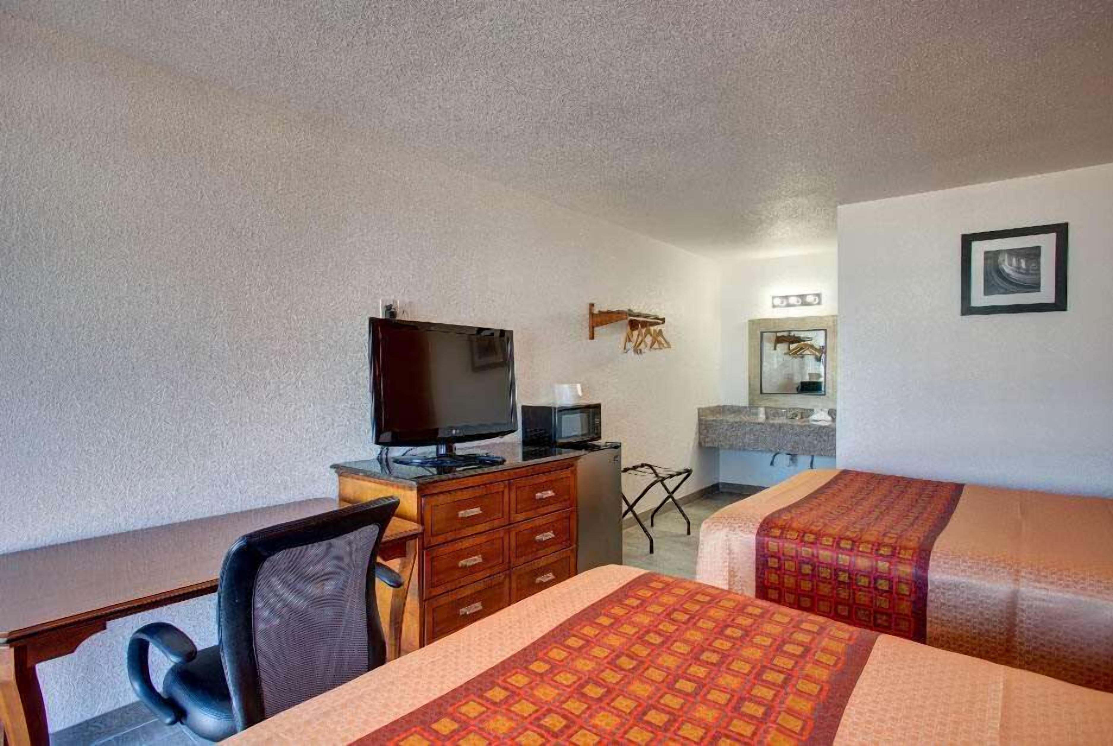 Une chambre d’hôtel avec deux lits, un bureau avec une télévision, une commode et un miroir.