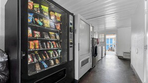 A hallway with a vending machine stocked with snacks and a refrigerator. - Motel 6 Branson, MO (Branson)