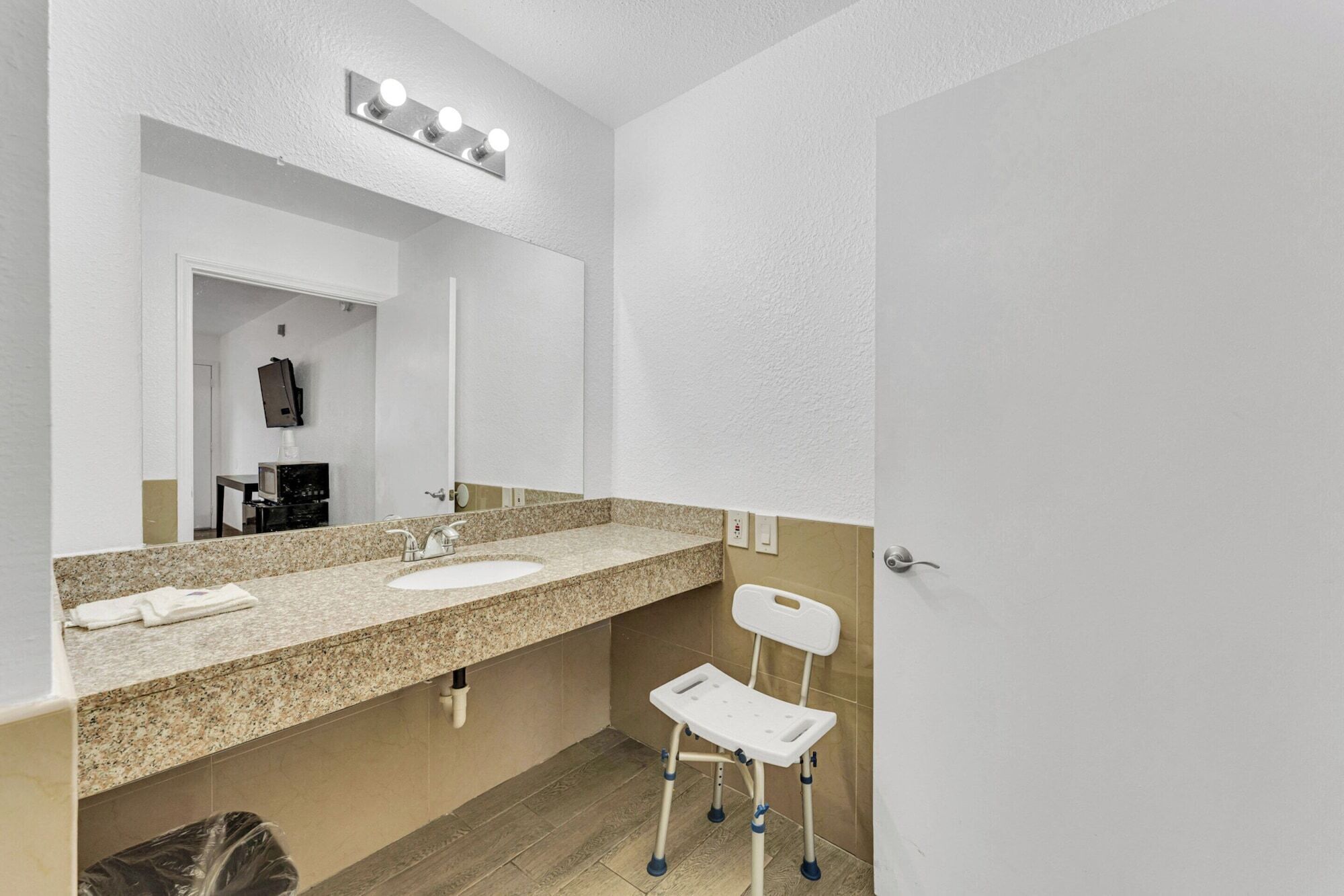 Un baño con encimera de granito, un lavabo, un espejo y una silla blanca.