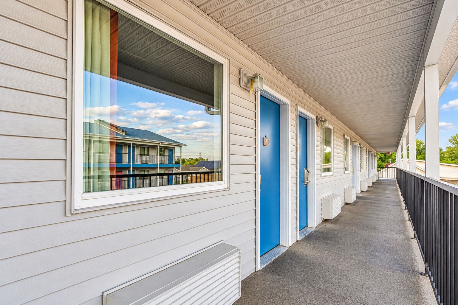 A motel with a covered walkway, individual rooms with doors, and a window with a view of a building.