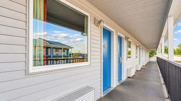 A motel with a covered walkway, individual rooms with doors, and a window with a view of a building.