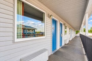 A motel with a covered walkway, individual rooms with doors, and a window with a view of a building. - Motel 6 Branson, MO (Branson)