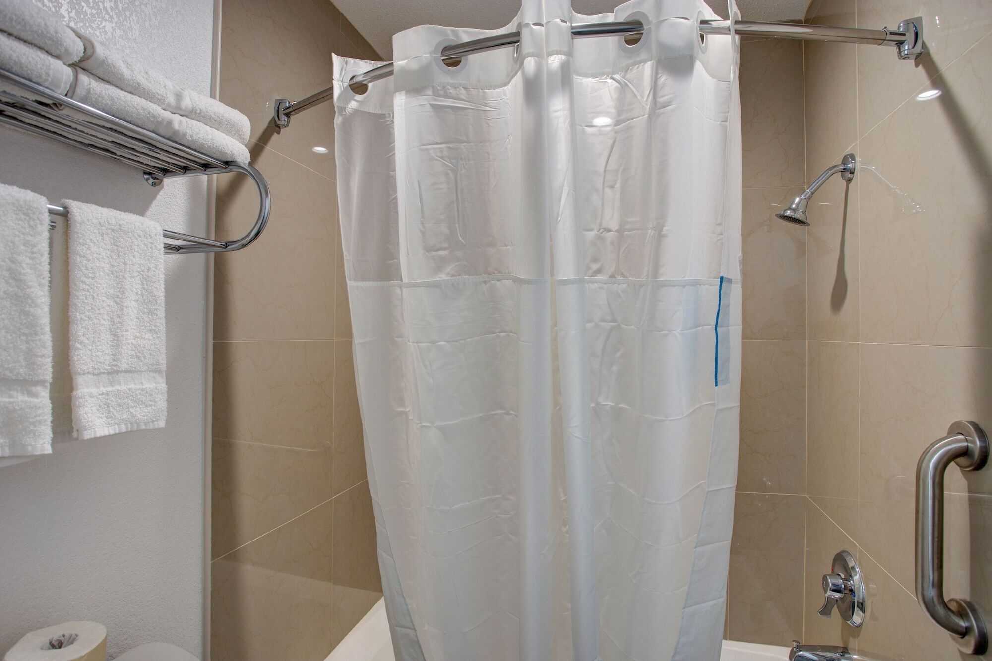 Un baño con cortina de ducha, un perchero con toallas, un inodoro y un pasamanos.