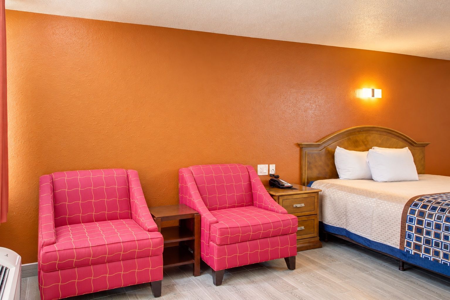 A hotel room with a bed, two armchairs, a nightstand, and a wall-mounted light.