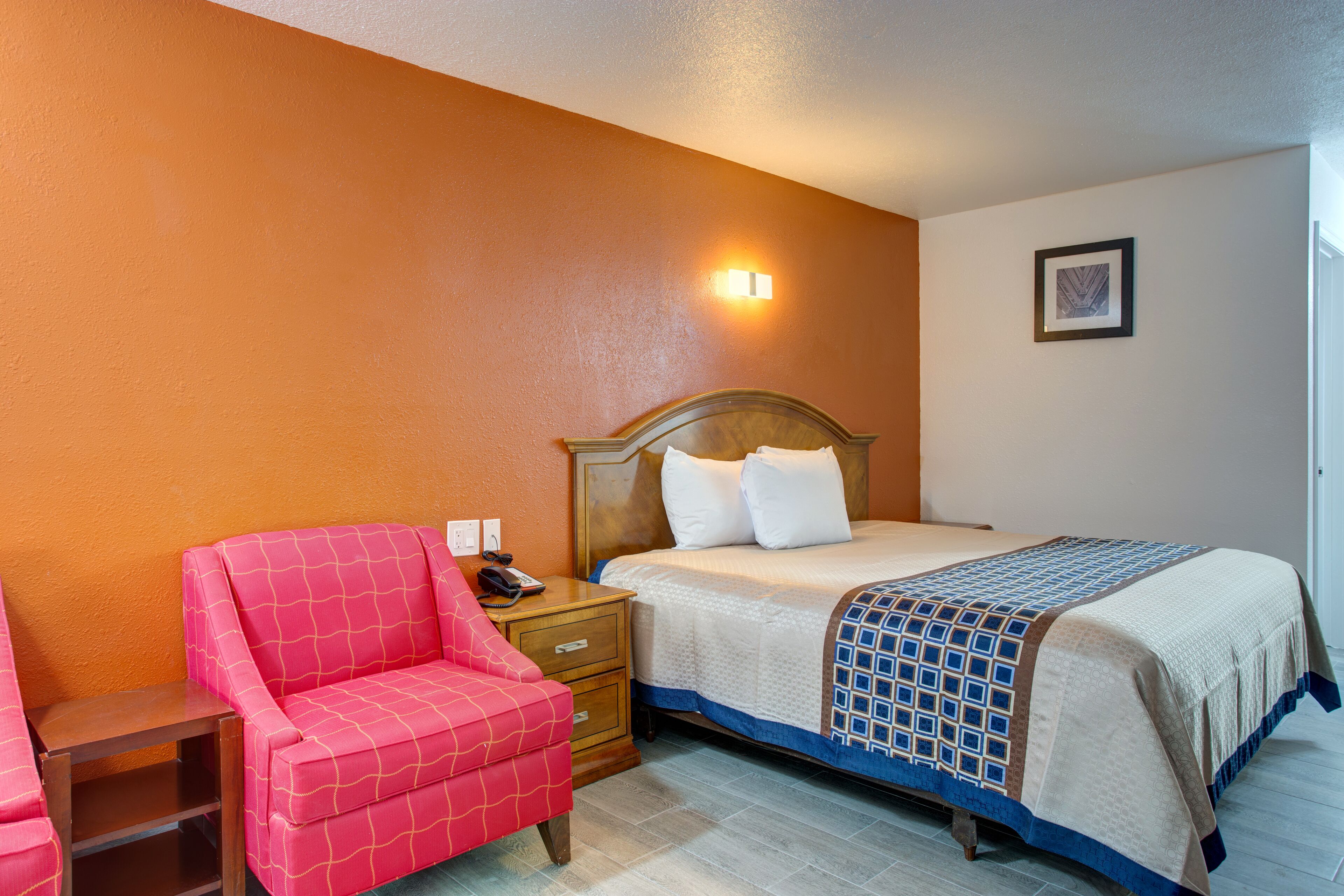 A hotel room with a bed, a nightstand, a red armchair, and a wall-mounted light.