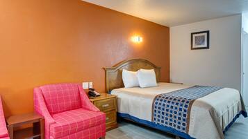 Une chambre d’hôtel avec un lit, une table de chevet, un fauteuil rouge et une lampe fixée au mur.