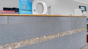 A reception desk with a large number '6' sign, a blue informational poster, and a digital screen. - Motel 6 Branson, MO (Branson)