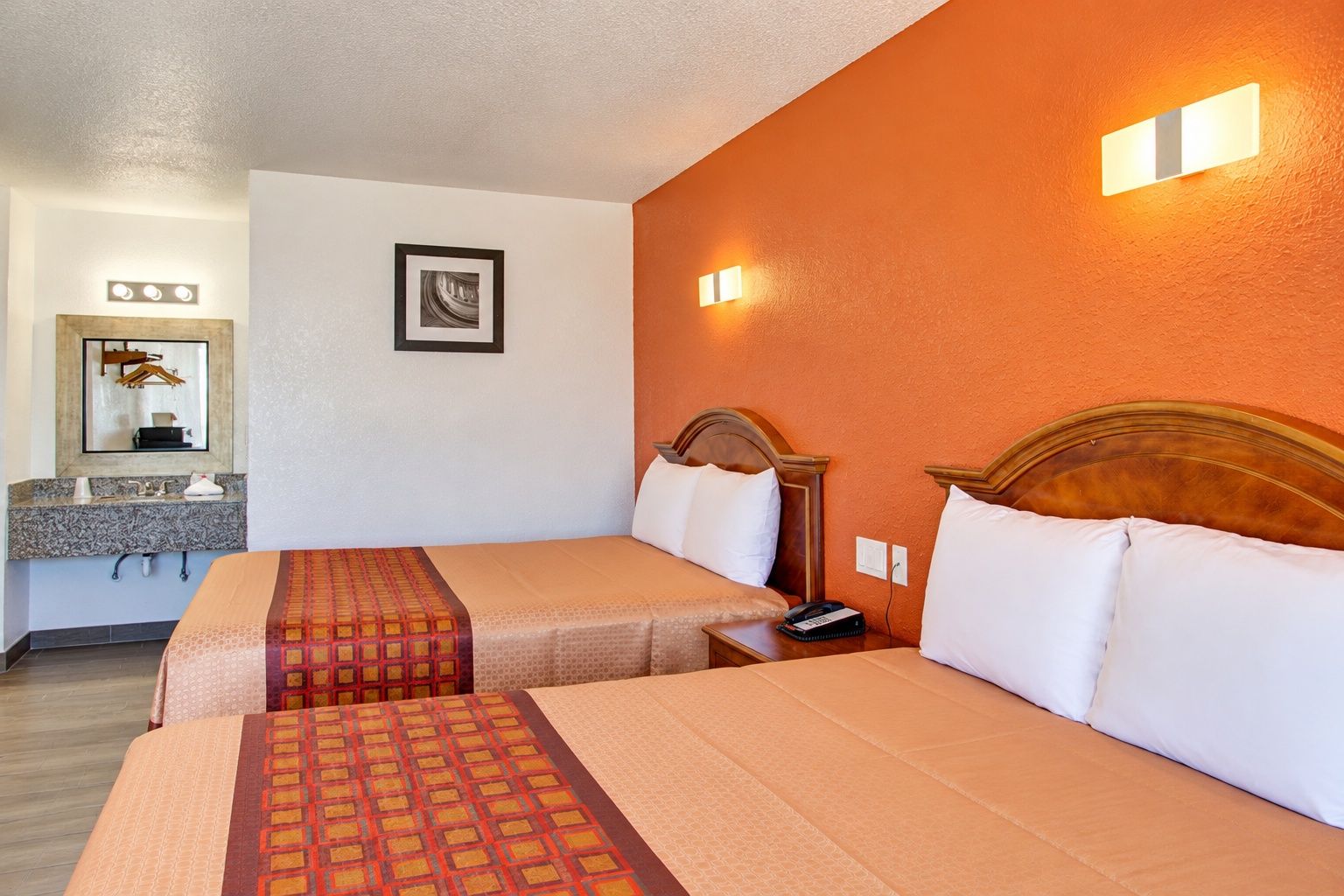 Une chambre d’hôtel avec deux lits, une salle de bain avec un miroir et un lavabo, et un luminaire fixé au mur.