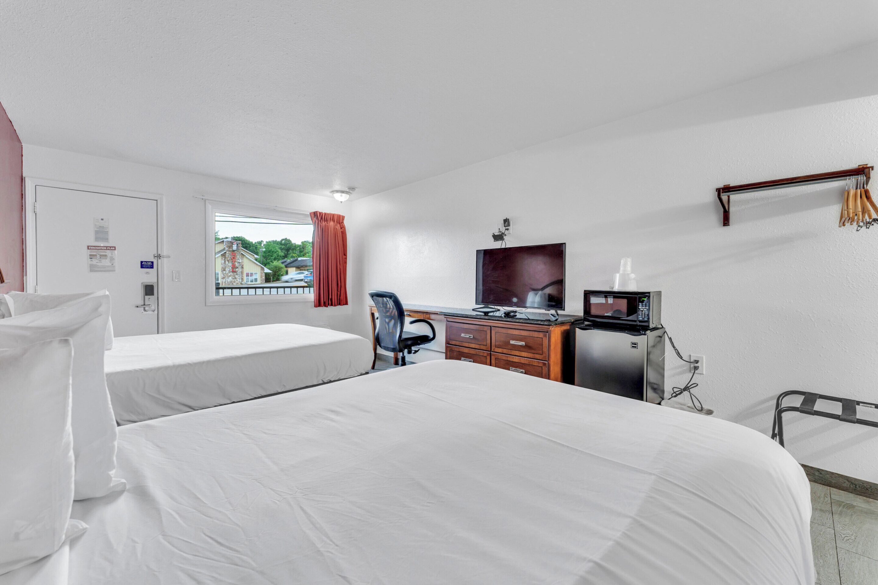 Ein Hotelzimmer mit zwei Betten, einem Schreibtisch mit Computer, einem Fernseher und einer Mikrowelle.