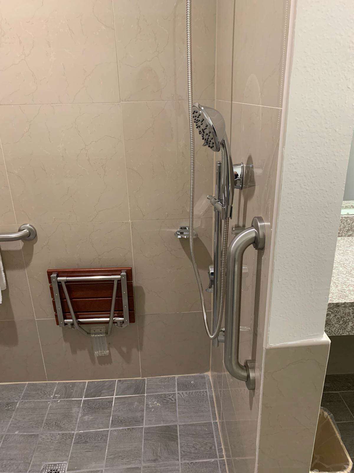 Un espace douche équipé d’un pommeau de douche à main, d’un panneau de commande fixé au mur et d’un porte-serviettes en bois.