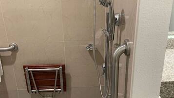 Un espace douche équipé d’un pommeau de douche à main, d’un panneau de commande fixé au mur et d’un porte-serviettes en bois.