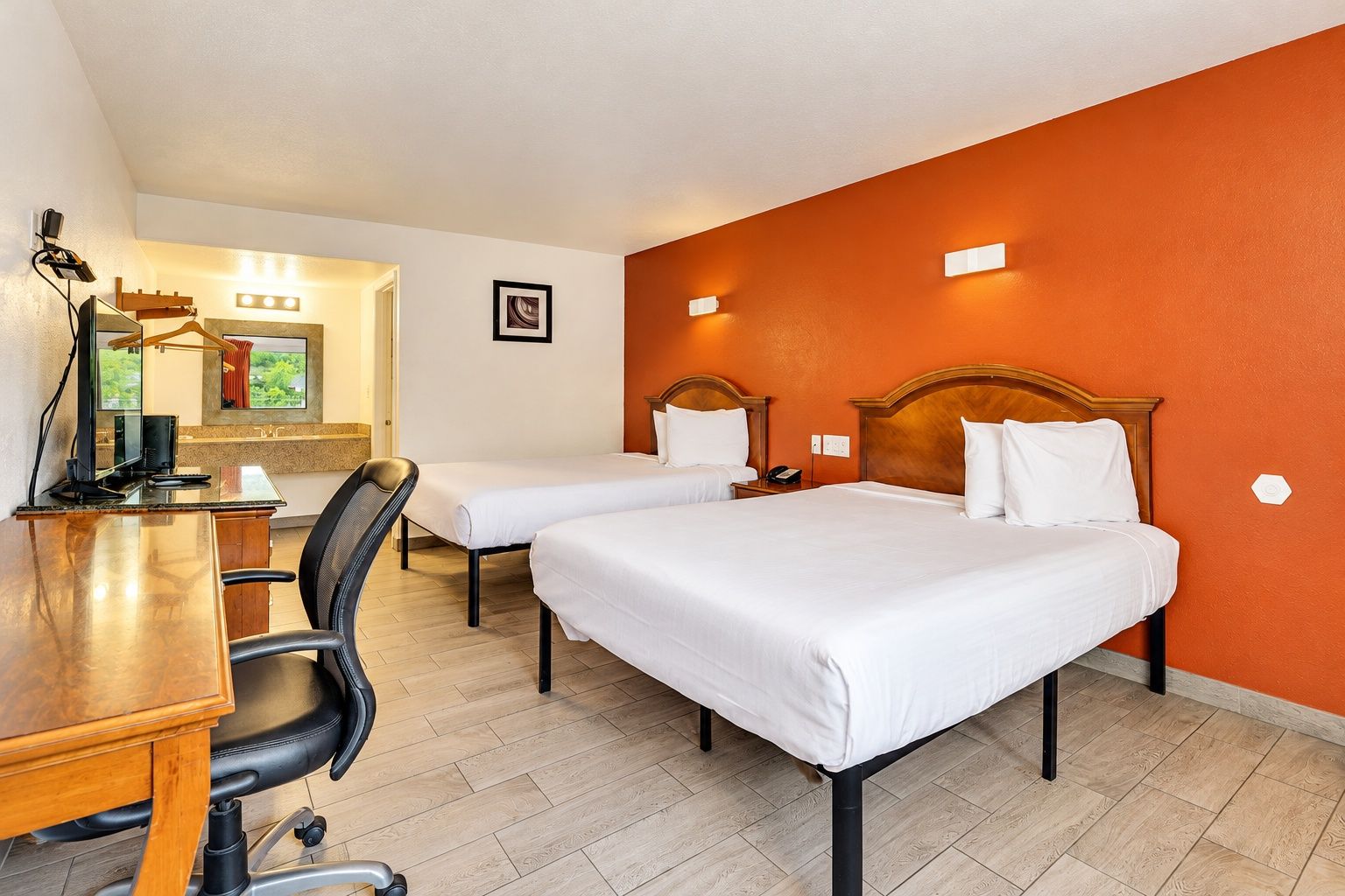 A hotel room with two single beds, a desk with a computer, and a chair.