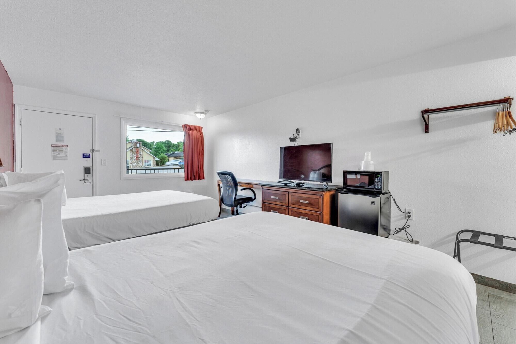 Habitación de hotel con dos camas, un escritorio con computadora y microondas, televisión y ventana con vista al exterior.