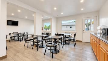 A spacious dining area with multiple tables and chairs, a kitchen area with a microwave, and a large window providing a view of the outside.
