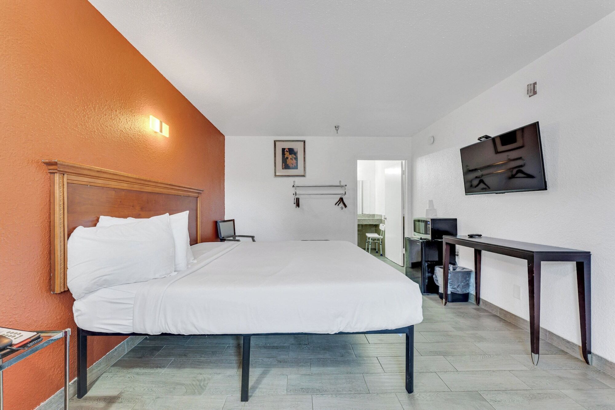 Habitación de hotel con una cama, un escritorio, una silla, un televisor y un baño visible a través de una puerta abierta.