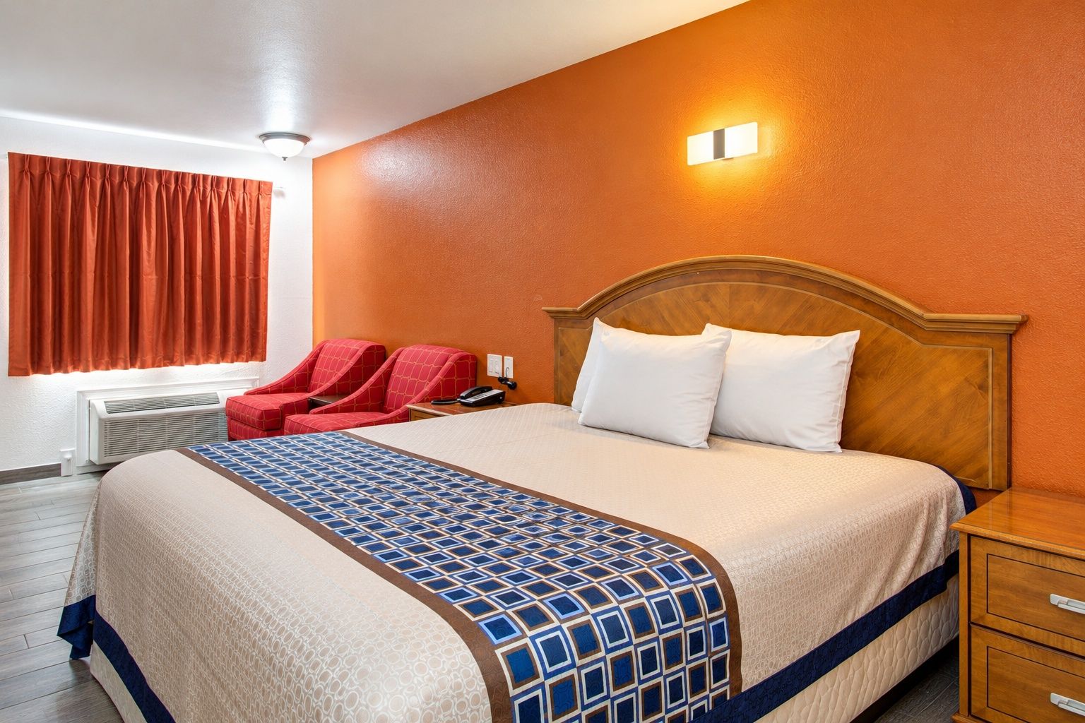 A hotel room with a large bed, a wooden headboard, a red sofa, and a wall-mounted light fixture.
