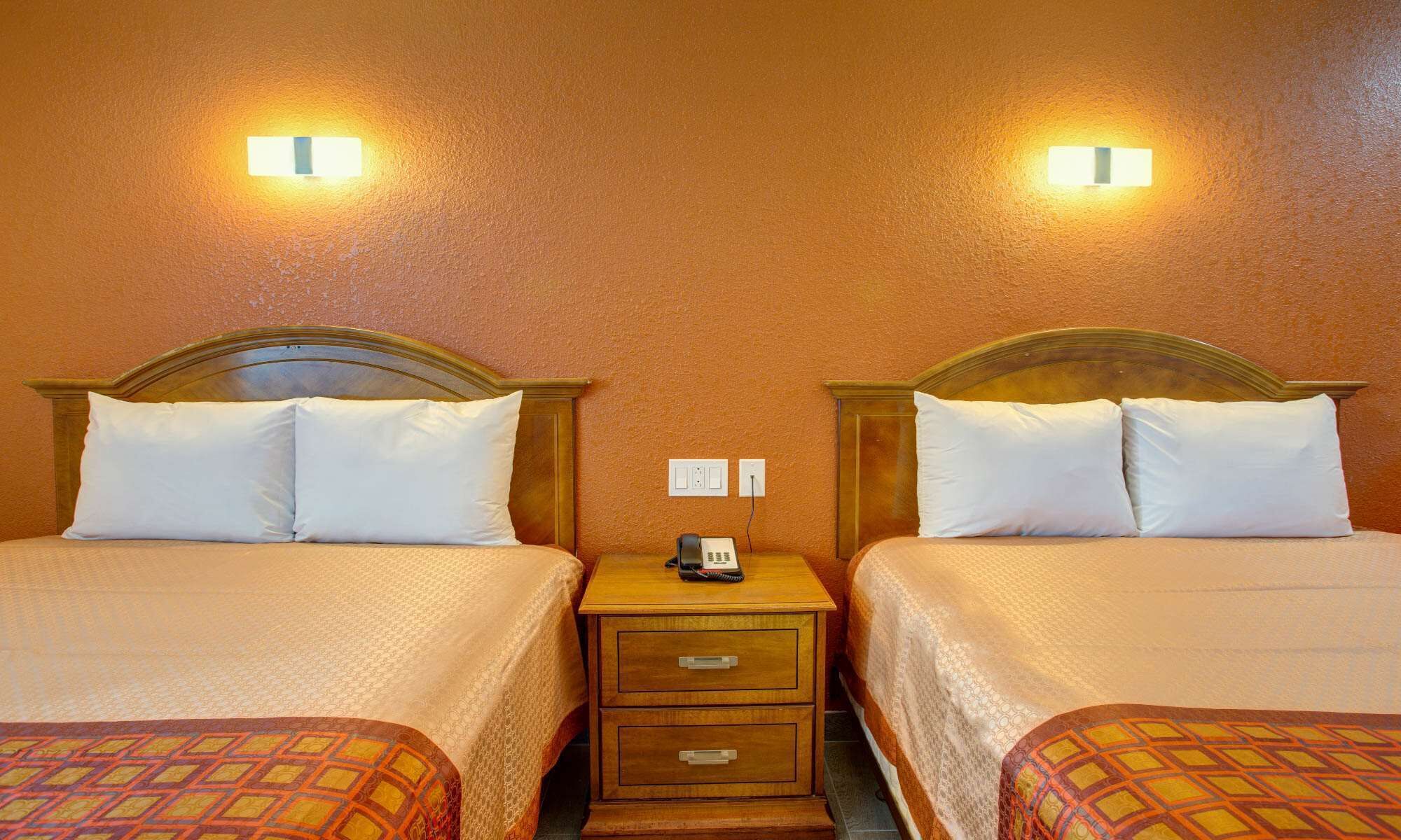 Una habitación de hotel con dos camas, cada una con cabecero, mesita de noche con teléfono y lámpara de pared.