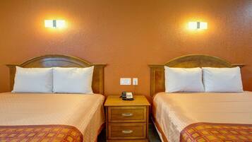 Una habitación de hotel con dos camas, cada una con cabecero, mesita de noche con teléfono y lámpara de pared.