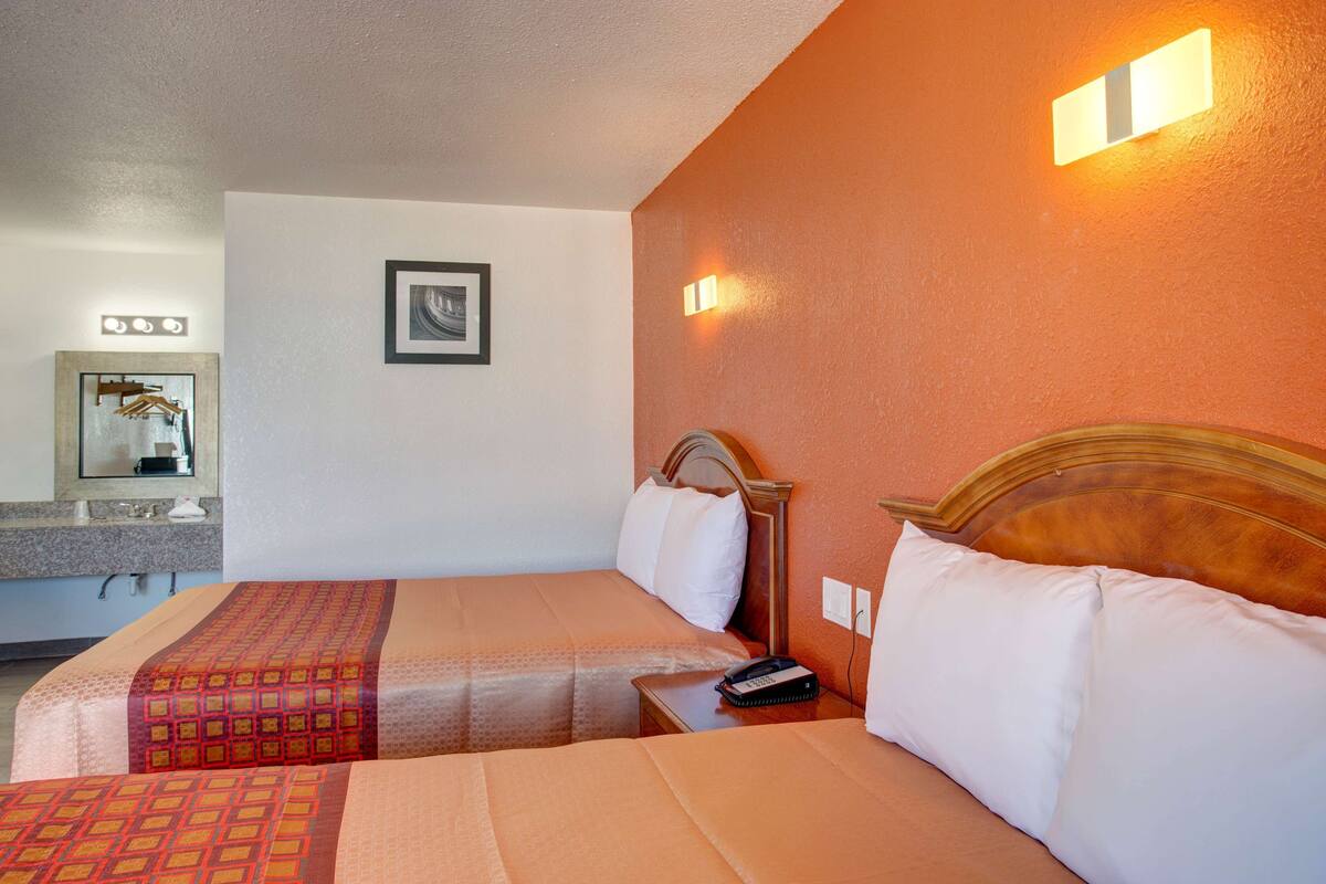 A hotel room with two beds, a bathroom, and a mirror.