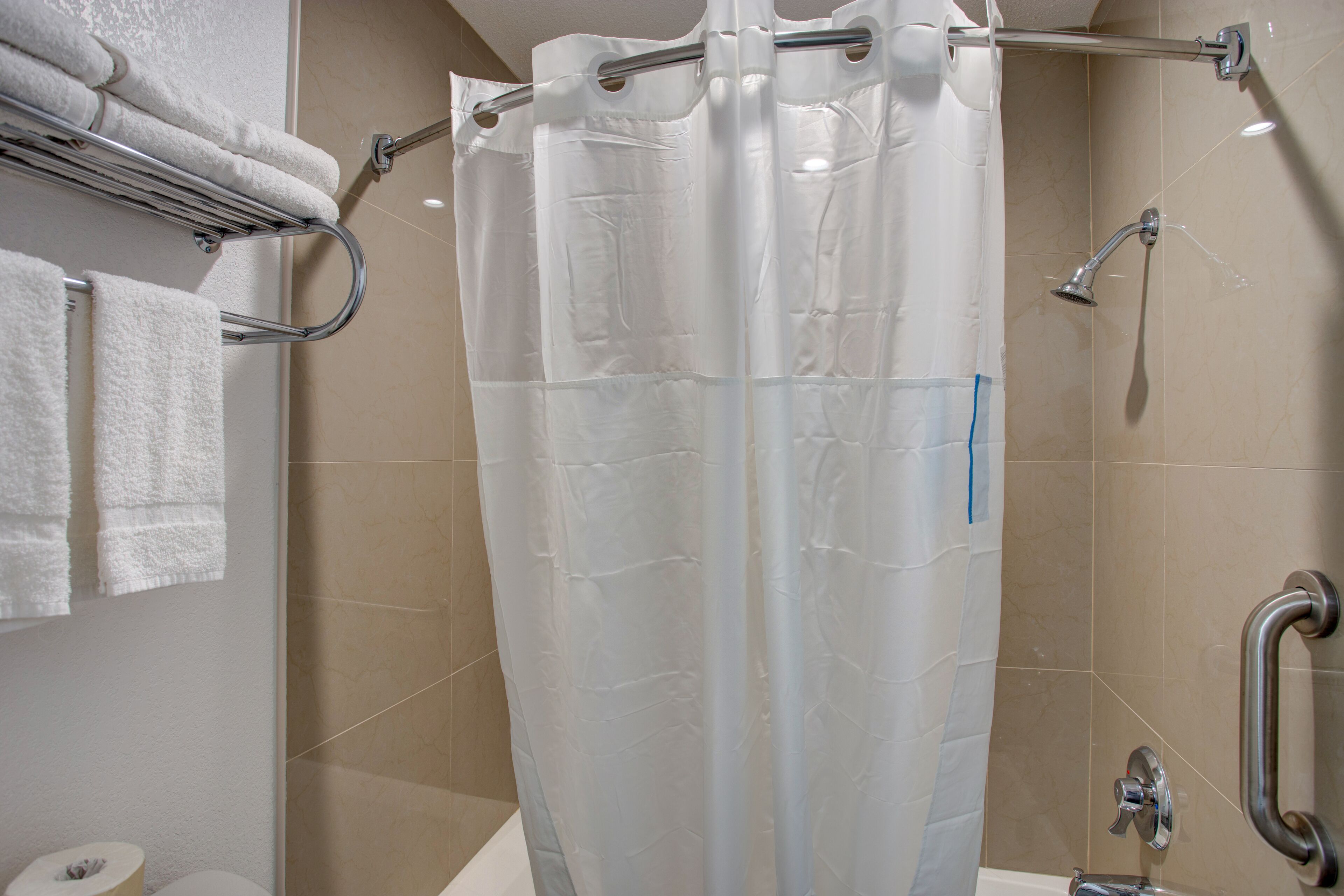 Een badkamer met douchegordijn, handdoekrek met opgevouwen handdoeken, toiletpapierhouder en bedieningspaneel voor de douche.