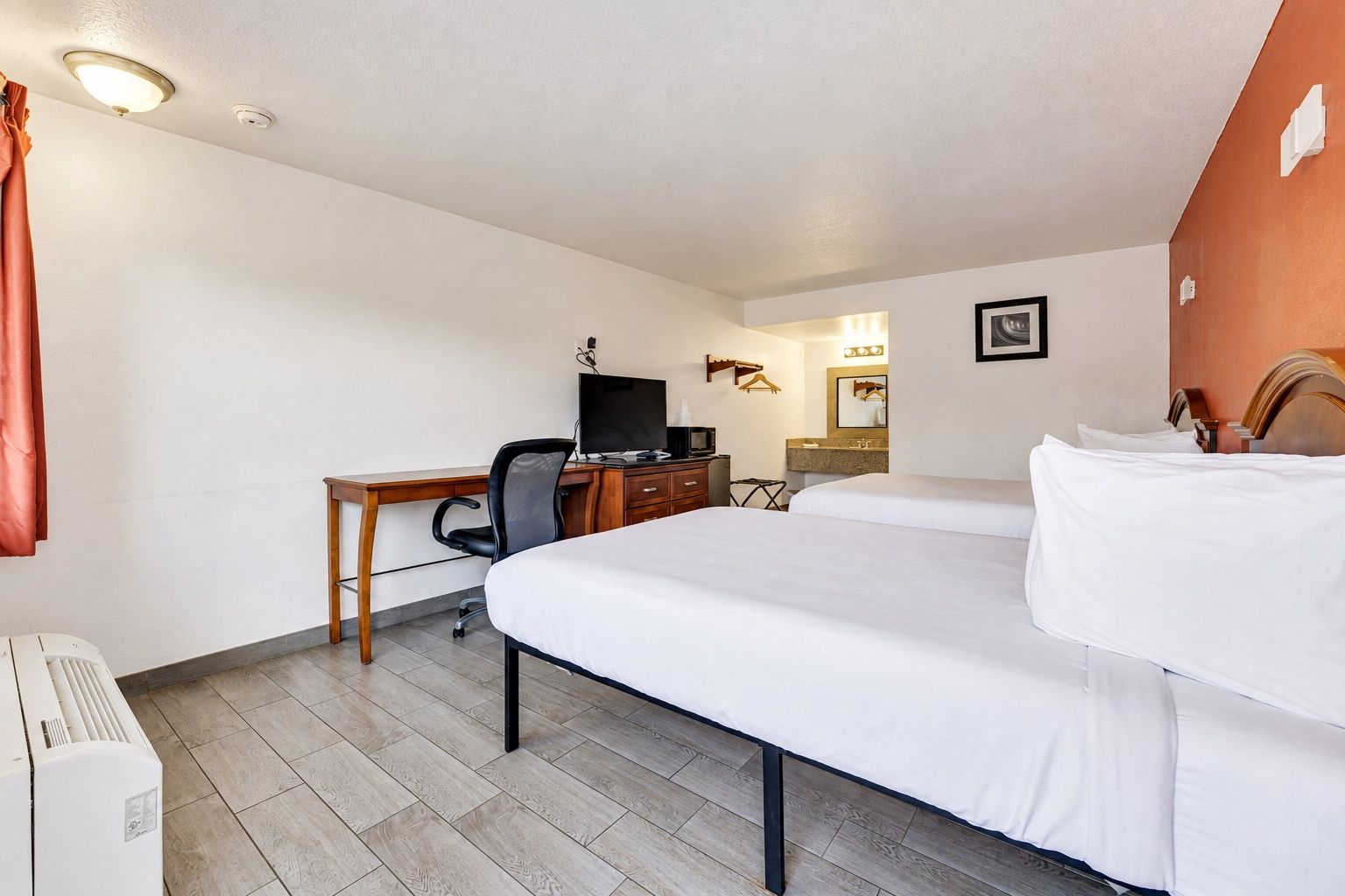 A hotel room with a bed, a desk with a chair, a television, and a bathroom mirror.
